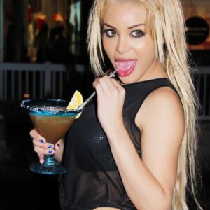 Beautiful blonde shemale Karla Carrillo sips a mixed drink on a patio while clothed