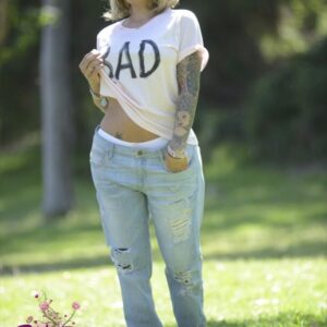 Transsexual model Foxxy poses outdoors for a SFW shoot in a T-shirt and ripped jeans