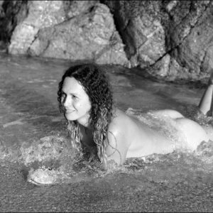 Trans female Nikki Montero sports curly brunette hair while naked in the ocean