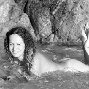 Trans female Nikki Montero sports curly brunette hair while naked in the ocean